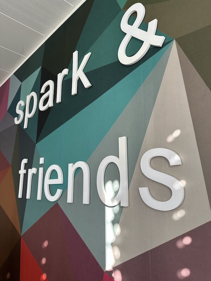 Schriftzug der addmore friends und der addmore spark an der bunt gestalteten Wand im neuen Büro